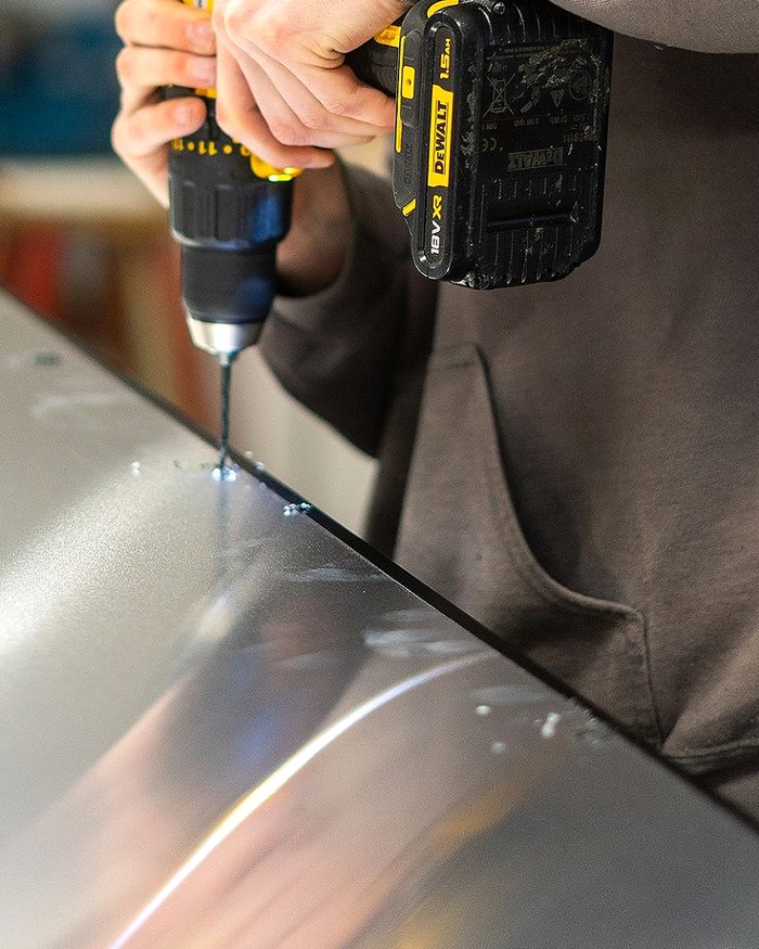 Handheld drill working on a metal sign panel